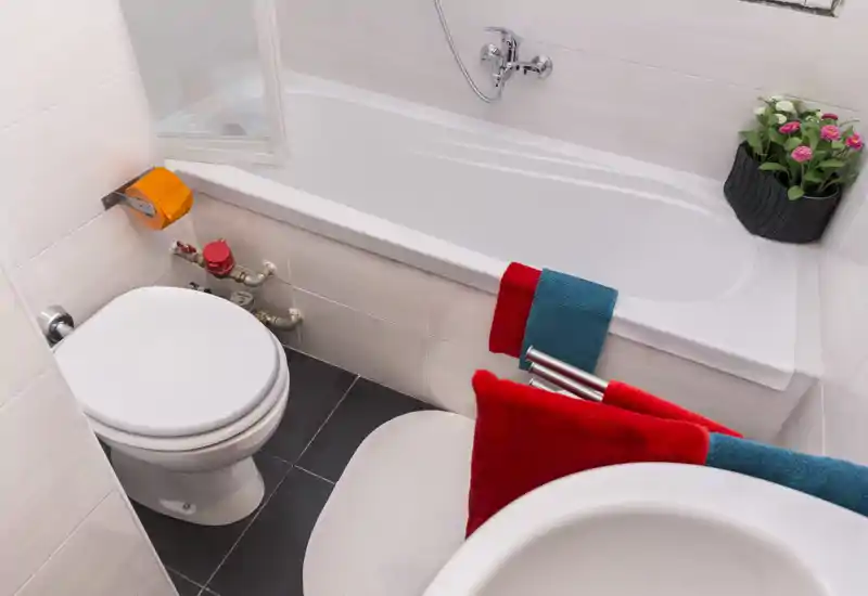 Compact, clean bathroom with a bathtub, toilet and sink; colorful towels and a small plant add a cheerful touch.