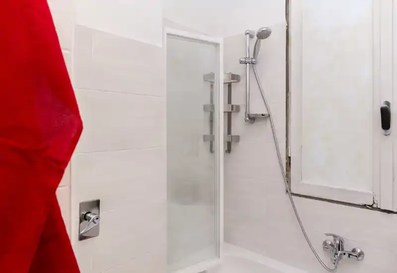 Small tiled bathroom with a showerhead, glass shower screen, bathtub fixtures and a frosted window; clean, simply styled space.