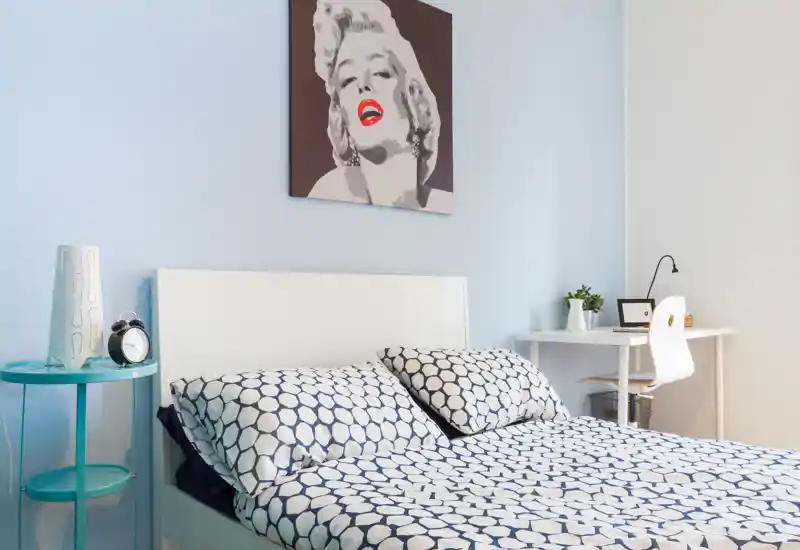 Dormitorio moderno y luminoso con cama completa, ropa de cama estampada, mesita y pequeño escritorio — estiloso, espacioso y bien iluminado.