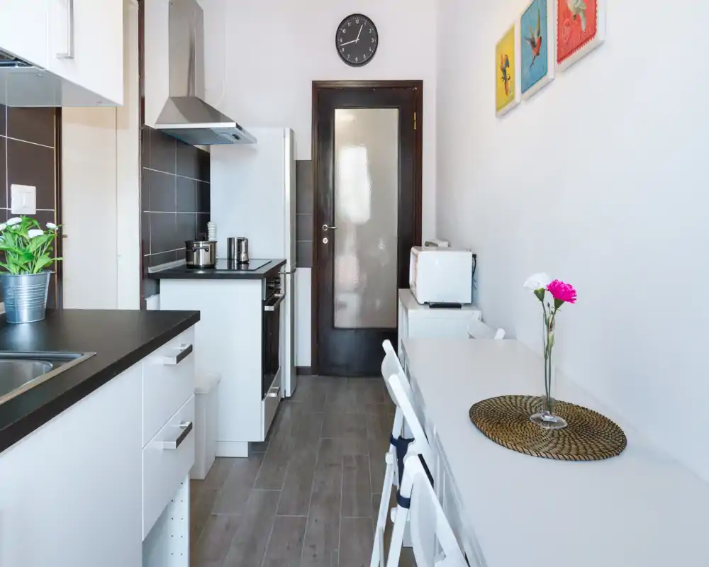 Cocina moderna y compacta con encimera negra, placa integrada y pequeño comedor; luminosa, limpia y bien organizada — ideal para un apartamento de corta estancia.
