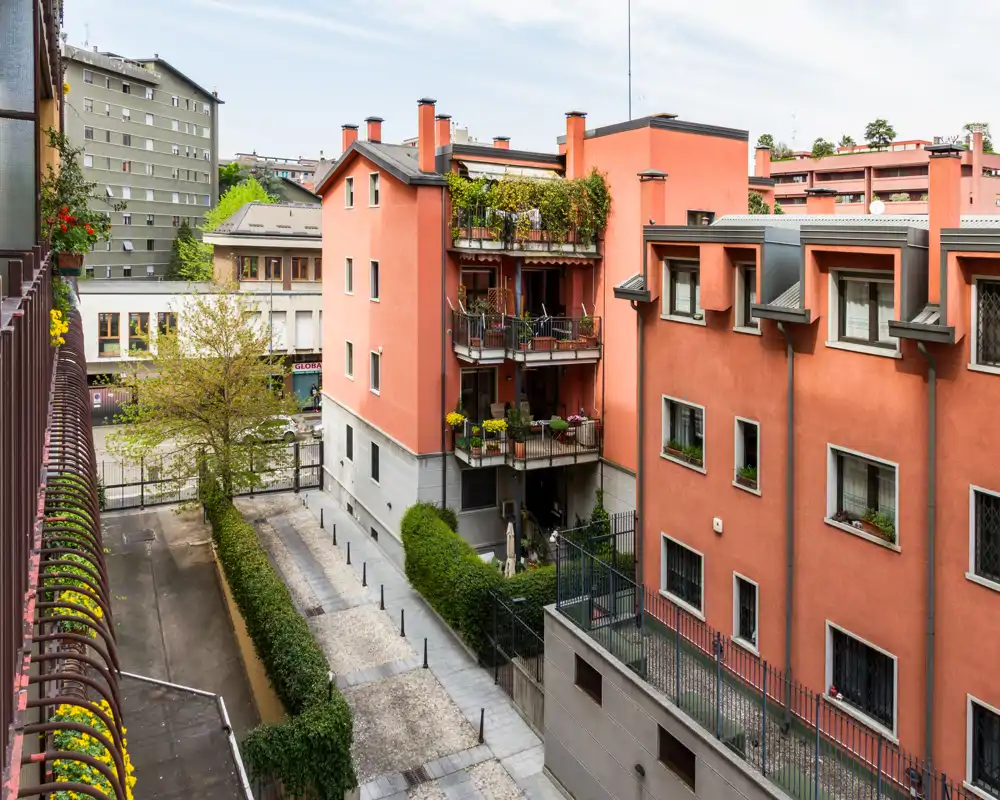 Vista del patio exterior y balcones con edificios color terracota, pasarela empedrada y balcones con plantas; imagen luminosa y bien encuadrada ideal para mostrar espacios exteriores comunitarios.