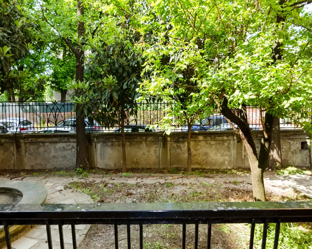 Pequeño jardín privado o patio con árboles, un muro bajo de piedra y un camino pavimentado; espacio verde agradable visible desde una barandilla.