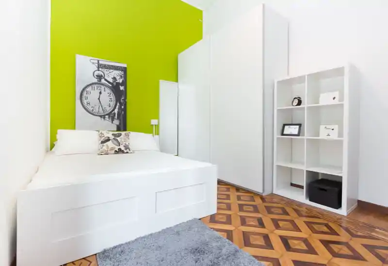 Chambre moderne et lumineuse avec lit blanc sur estrade devant un mur vert vif, parquet géométrique et étagère blanche — présentation soignée idéale pour une annonce.