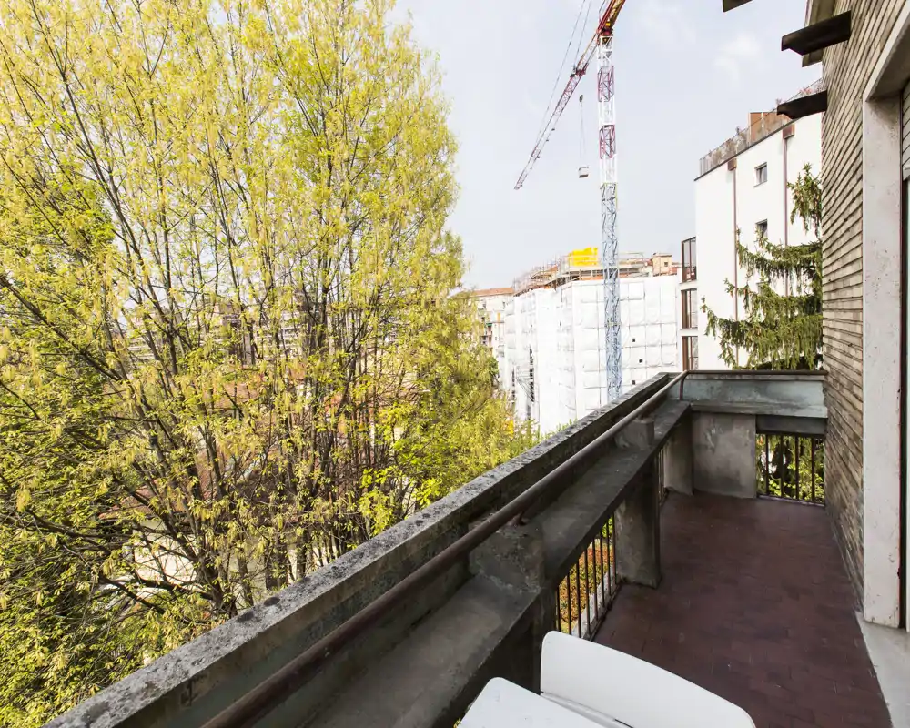 Sunny private balcony with a city view framed by mature trees — tiled floor and a concrete balustrade offer a quiet outdoor spot.