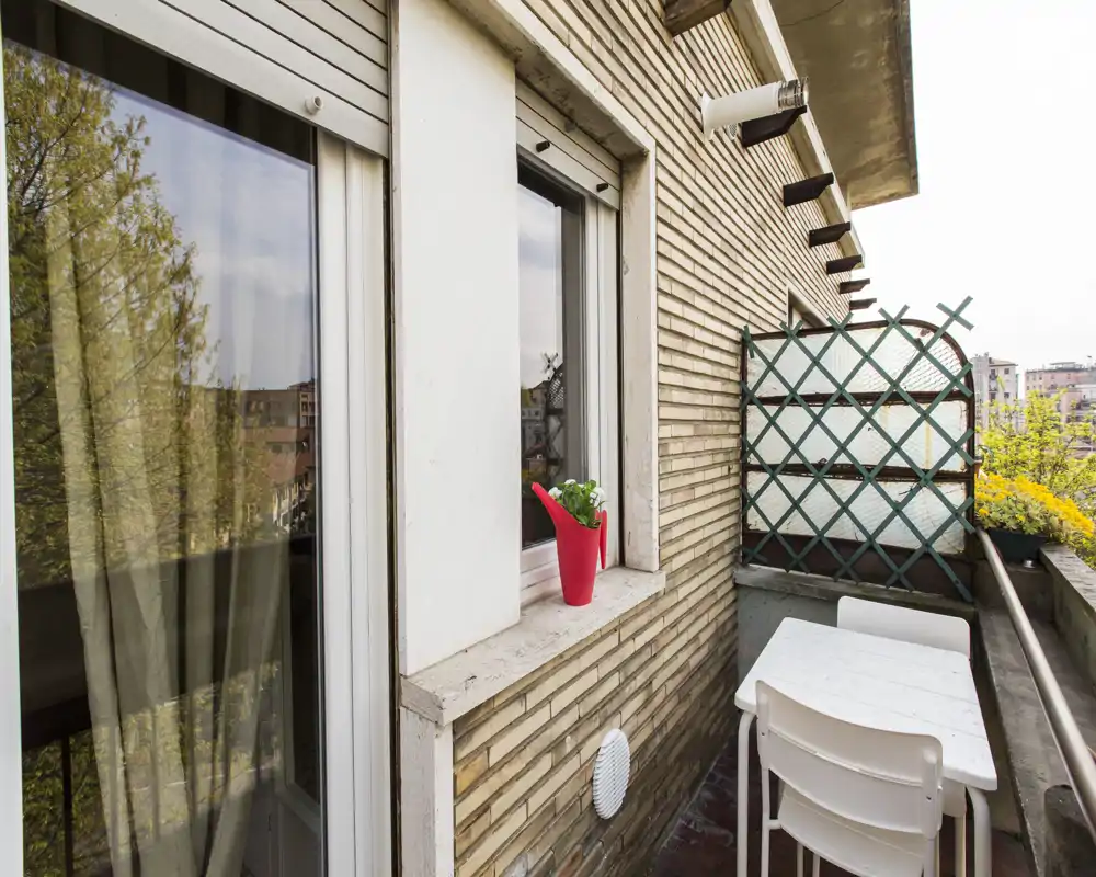 Sunny balcony with a small white table and chairs, decorative trellis and potted plants — ideal for morning coffee with a view.