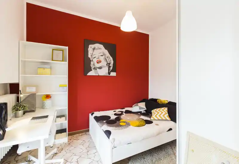 Bright, stylish single bedroom with a patterned bed, bold red accent wall and a compact workspace — ideal for a comfortable stay.