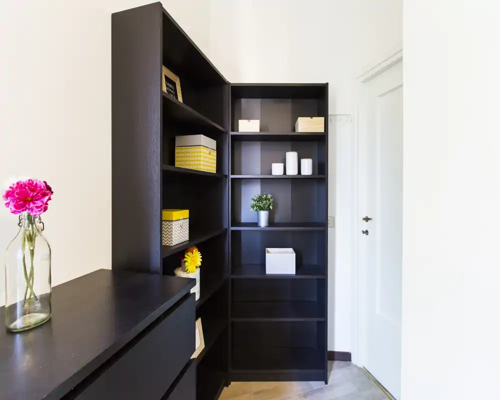 Bright, tidy entrance area with dark shelving units and a small decorative vase; neutral walls and a white entrance door create a welcoming first impression.