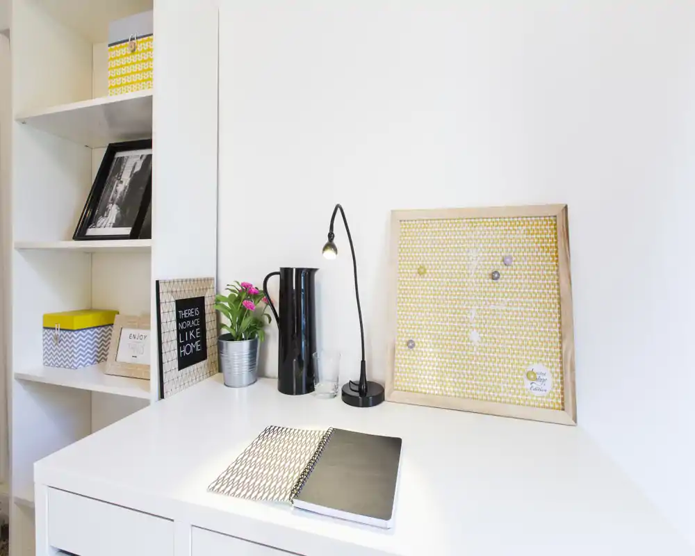 Bright, tidy desk corner with a lamp, small plant and framed decor — a compact workspace within the living area, perfect for focused work.