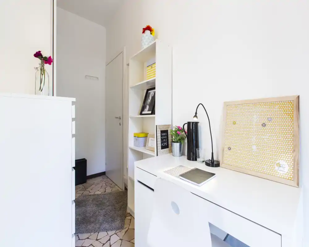 Bright, compact living area with a white desk, shelving and decorative accents creating a tidy workspace and entry corner.