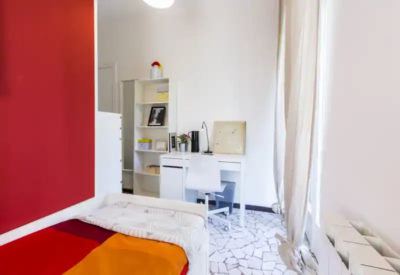 Bright, modern single bedroom with colorful bedding, a bedside study desk and large window letting in natural light — ideal for a student or single occupant.