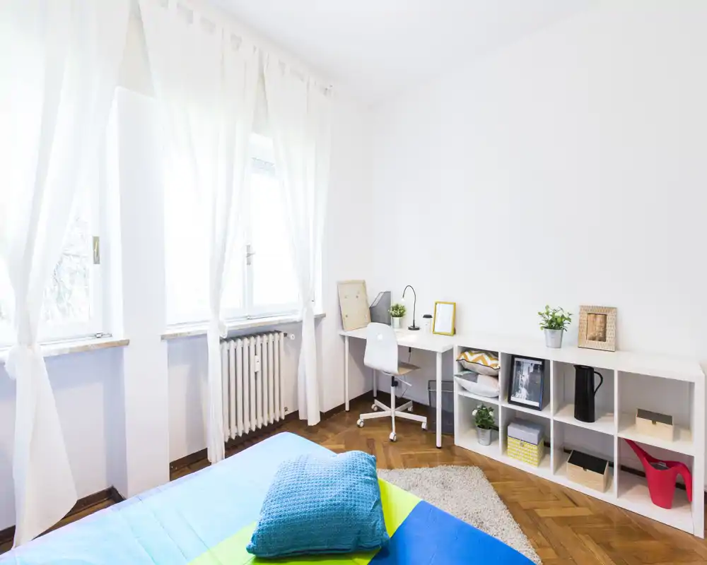 Camera da letto luminosa e moderna con letto ben rifatto, colori vivaci e una piccola scrivania vicino alla finestra, perfetta per affitti brevi.