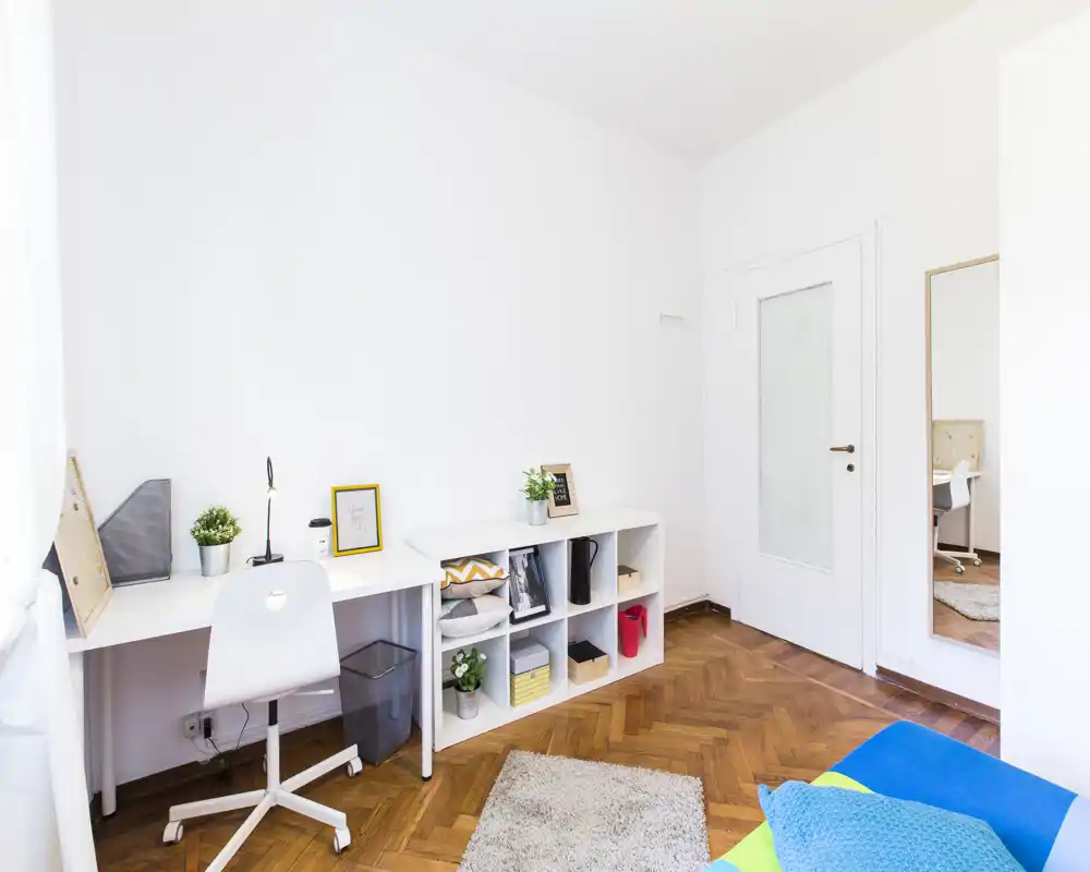 Area living luminosa e moderna con scrivania, scaffalatura, tappeto morbido e cuscini colorati — ideale per lavoro e relax in uno spazio compatto e di stile.