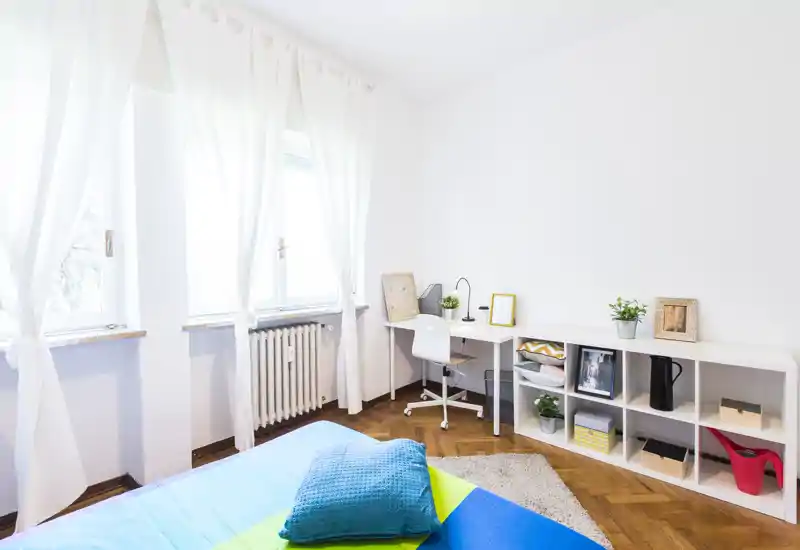 Camera da letto luminosa e moderna con letto ben rifatto, colori vivaci e una piccola scrivania vicino alla finestra, perfetta per affitti brevi.