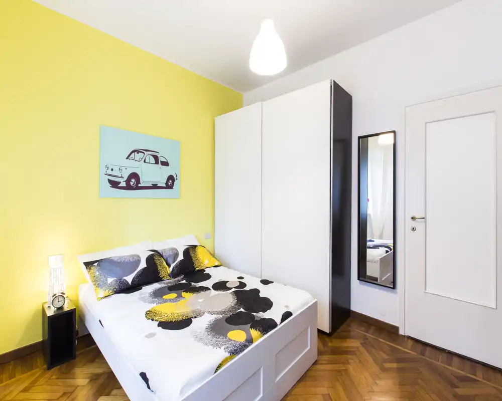 Dormitorio luminoso y moderno con cama doble, ropa de cama estampada y un gran armario — espacio acogedor y bien iluminado.