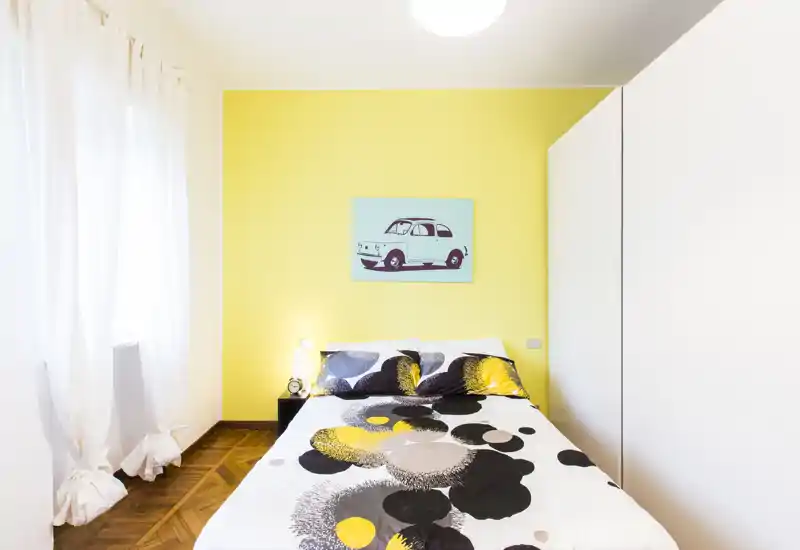 Dormitorio moderno y luminoso con cama doble, pared amarilla de acento y decoración sencilla y con estilo — ideal para estancias cortas.