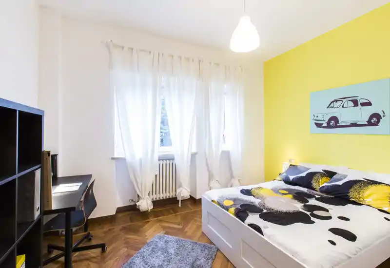 Dormitorio moderno y luminoso con cama doble confortable, pared de acento amarilla y una gran ventana que aporta luz natural.