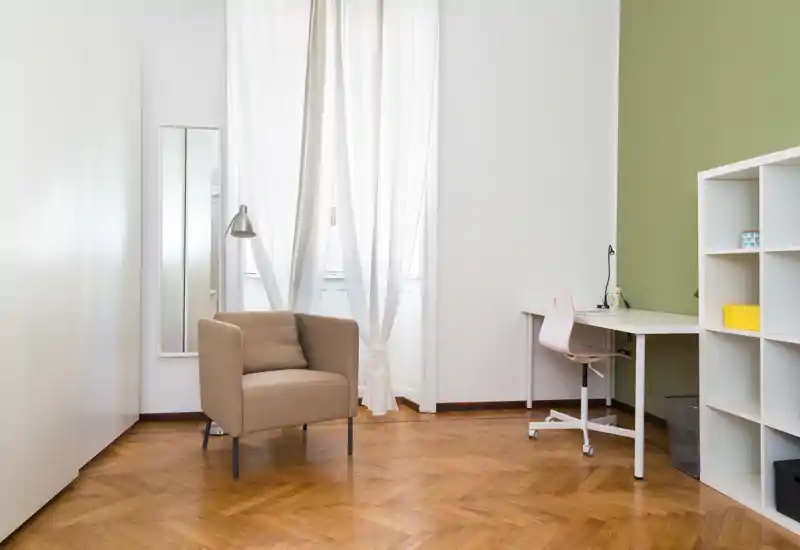 Bright, minimal living area with a comfortable single armchair, desk and shelving — ideal for relaxing or working in a compact space.