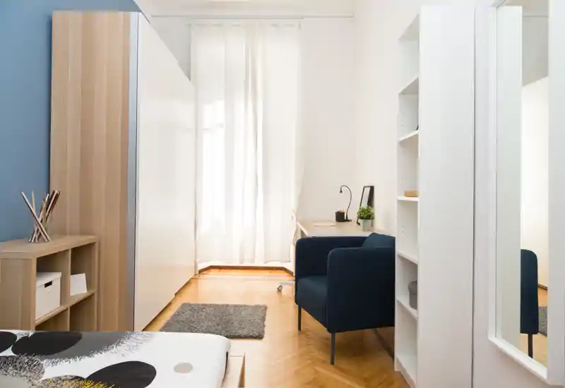 Camera da letto moderna e luminosa con letto ben visibile, poltrona accogliente e una piccola scrivania davanti alla finestra: ideale per soggiorni confortevoli.