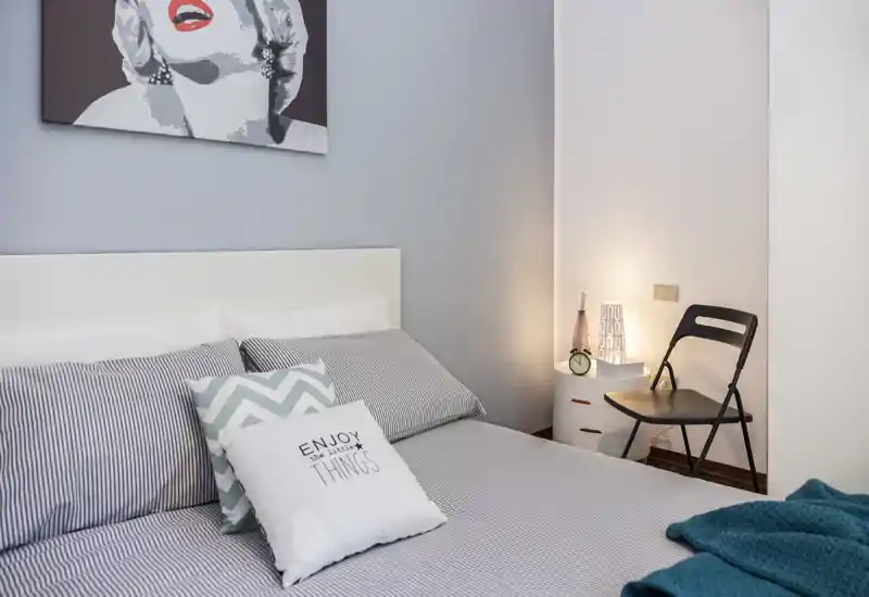 Chambre lumineuse et élégante avec un lit confortable, des coussins décoratifs et une lampe de chevet créant une ambiance chaleureuse.