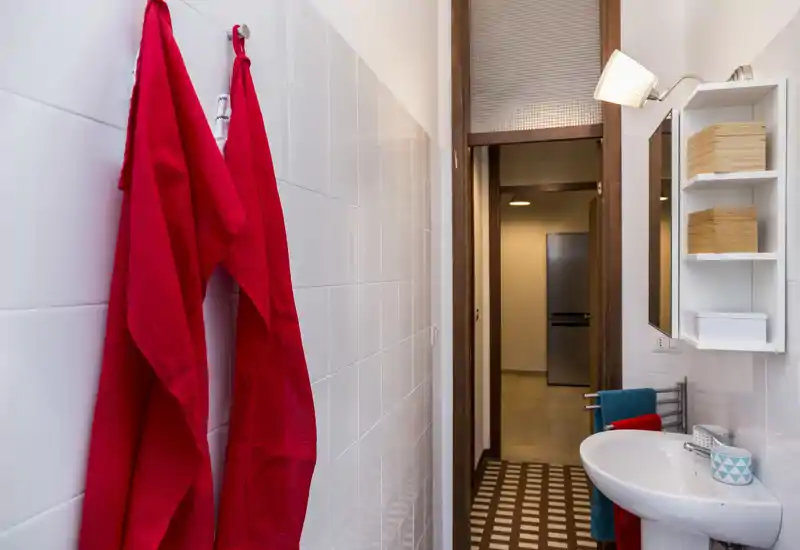 Compact, well-lit bathroom with white tiled walls, a washbasin, mirror cabinet and colorful towels adding contrast.