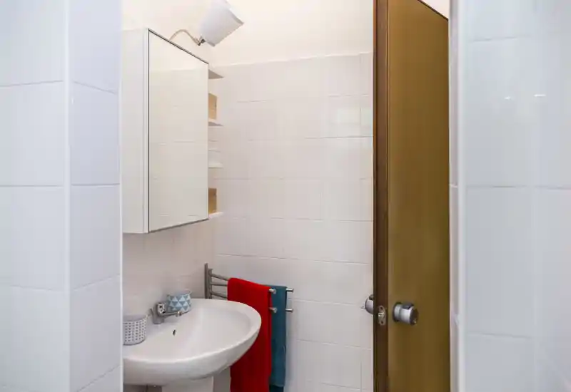 Compact, well-lit bathroom with a wall-mounted sink, mirror cabinet and towel rail with colorful towels.