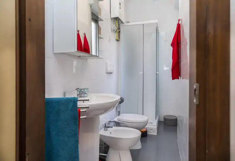 Compact, well-lit bathroom with shower cabin, bidet, toilet and sink; fresh towels and modern fixtures suitable for an apartment.