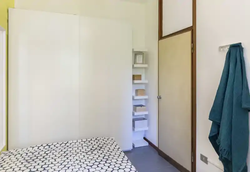 Chambre compacte avec housse de couette à motifs, armoire intégrée et étagères ouvertes — lumineuse, soignée et décorée simplement.