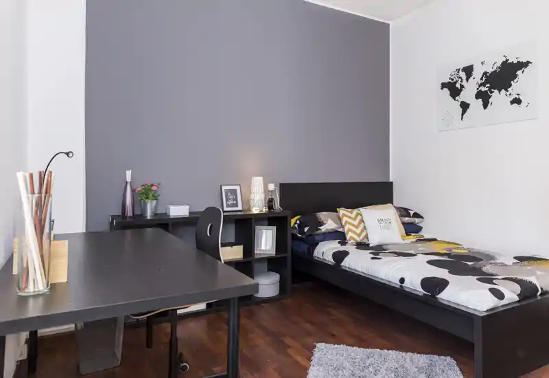 Dormitorio individual moderno y luminoso con cama baja negra, ropa de cama con estampado y escritorio. Decoración minimalista estilo nórdico, suelo de madera y mapa mural que crean un espacio acogedor y ordenado.