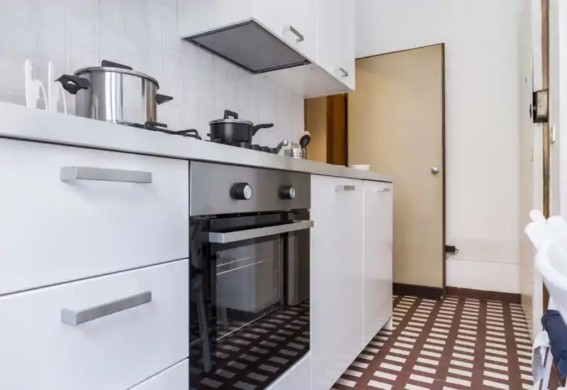 Bright, modern kitchen featuring a built-in oven, gas hob and white cabinetry with tiled backsplash — compact and well organized for efficient cooking.