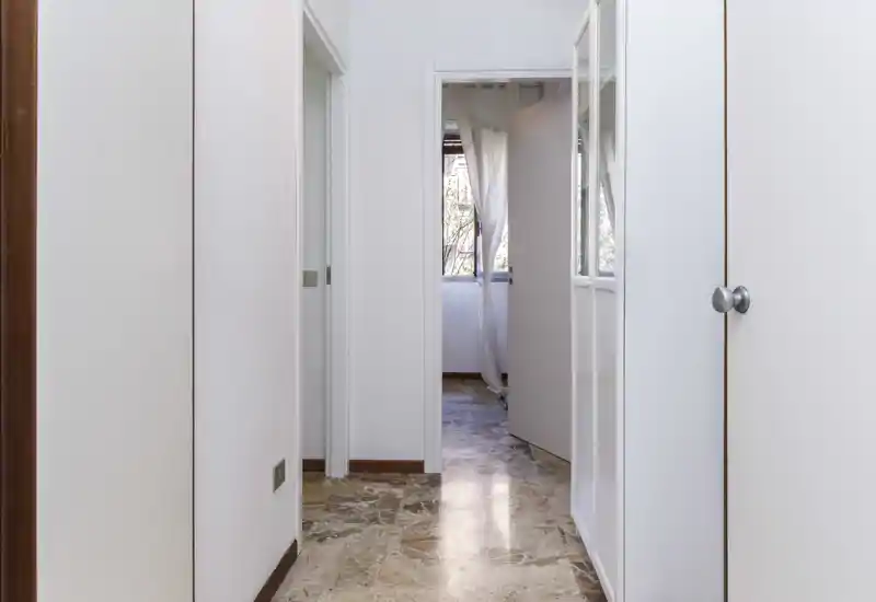 Bright, clean hallway/entrance with marble flooring, white walls and built-in storage; natural light comes through a doorway at the end.