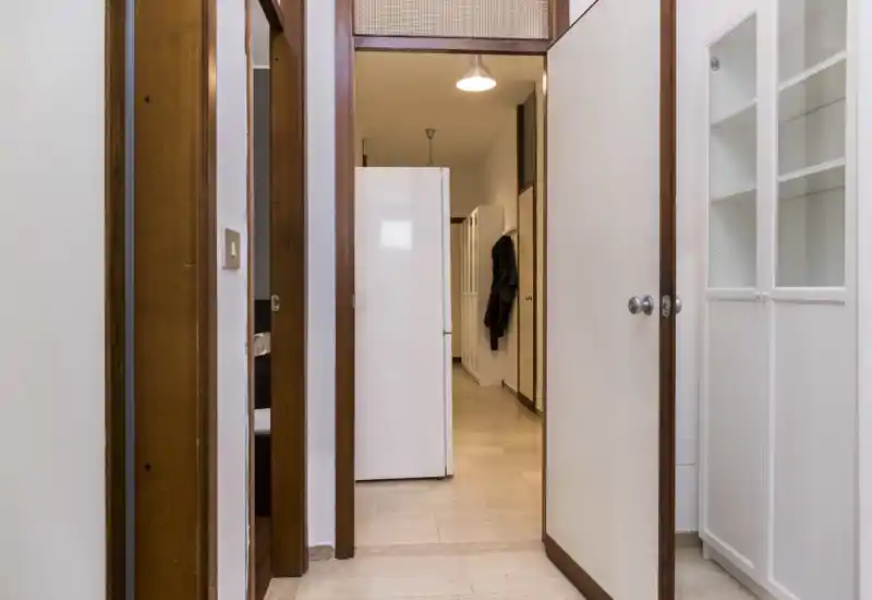 Neat internal entrance/hallway with open doors, tiled floor and built-in storage — a practical transition space connecting rooms.