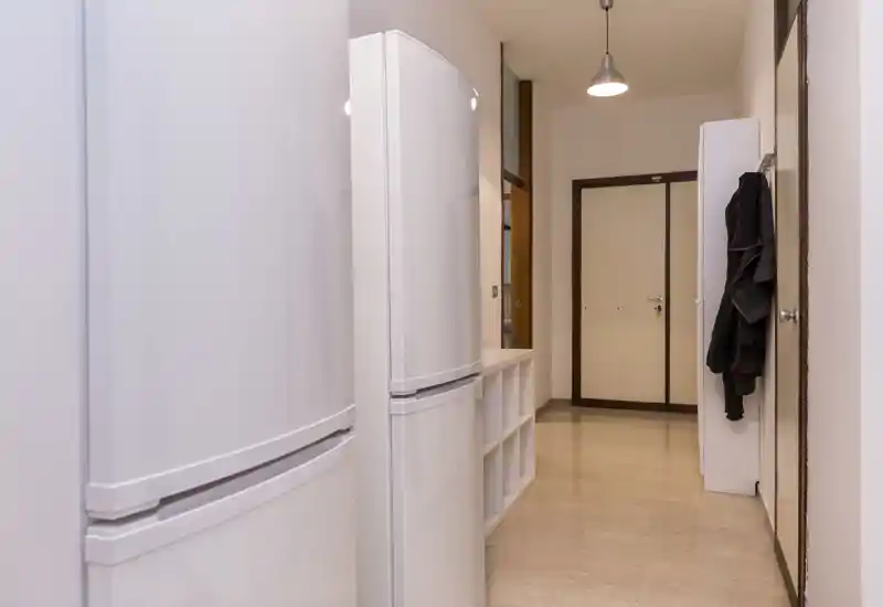 Simple, well-lit entrance corridor with storage units and coat hooks; neutral tones and clean floor create a functional arrival space.