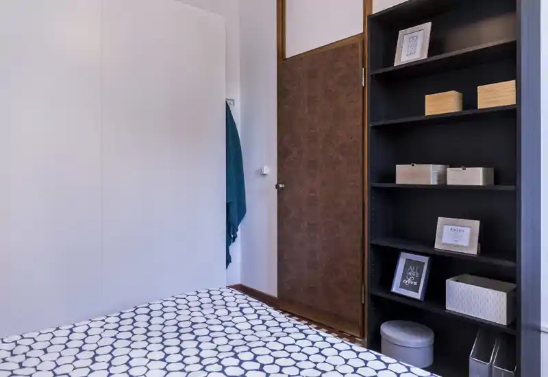 Coin chambre lumineux et soigné avec une couette à motifs et des étagères pour rangement et décoration ; lignes nettes et bois chaud pour une atmosphère accueillante.