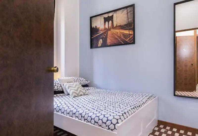 Chambre confortable et soignée avec lit double habillé de linge à motifs, coussins décoratifs et tableau mural; lumière douce et miroir plein pied apportent de la profondeur.