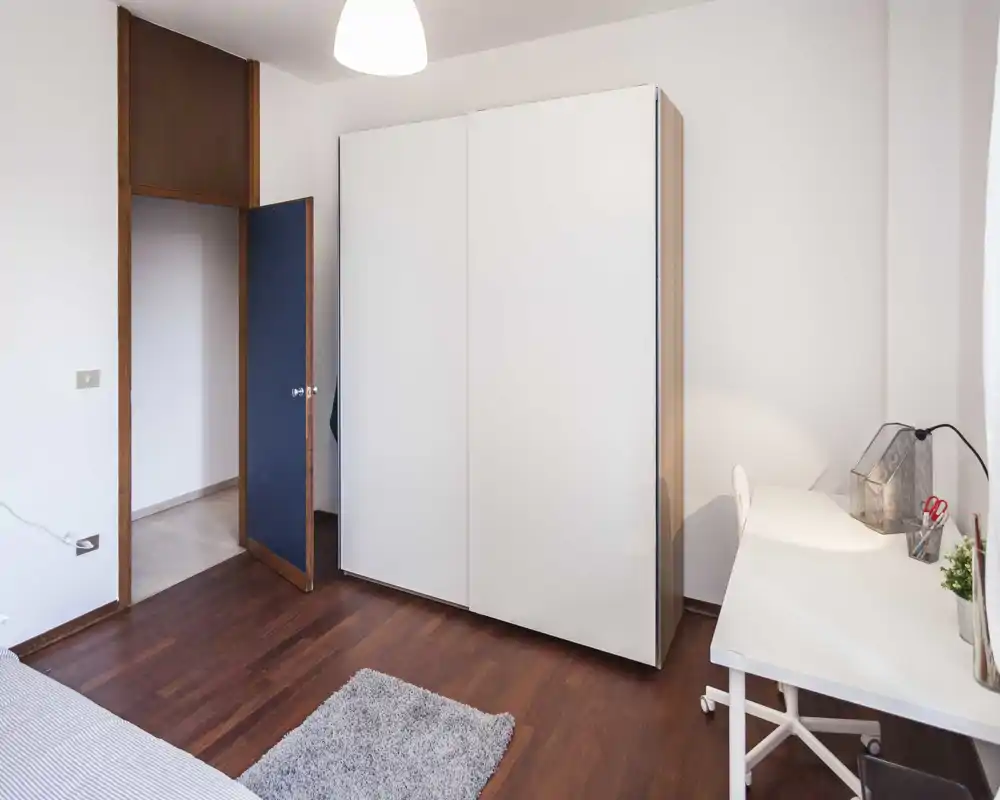 Pequeña entrada o pasillo con puerta visible y suelo de madera; la imagen está muy distorsionada por artefactos de compresión pero sugiere un espacio de paso.