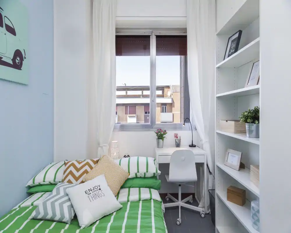 Camera da letto luminosa con un letto singolo/matrimoniale ben rifatto, cuscini decorativi e luce naturale che crea un’atmosfera ariosa.