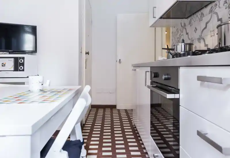 Compact modern kitchen with built-in oven and stove, patterned tile floor and a small dining table — bright, clean and well organized.