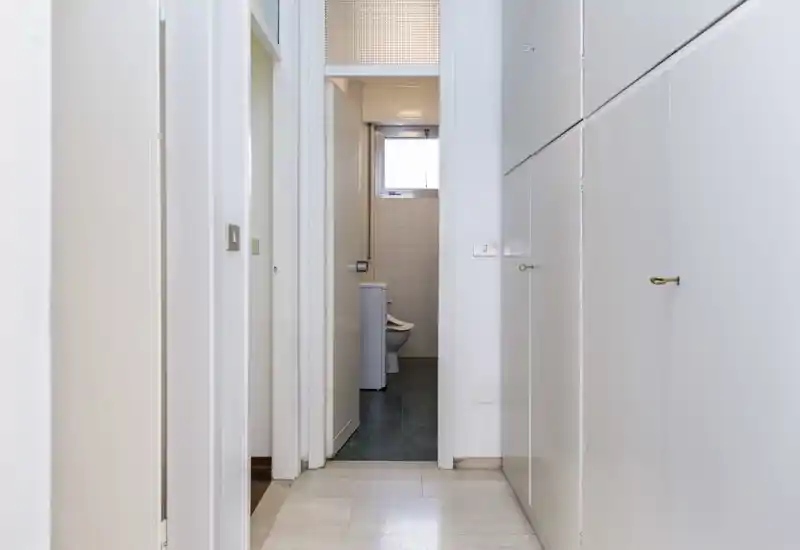 Bright, narrow entrance corridor with built-in storage and a view into a small bathroom at the end; neutral colors and even lighting make it practical for an apartment listing.