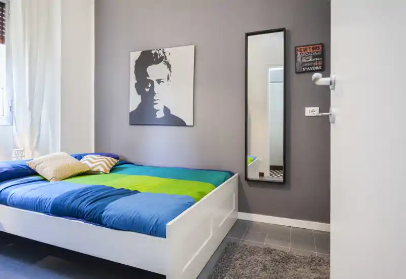 Bright, modern bedroom with a white platform bed dressed in colorful blue and green linens, decorative pillows and a large portrait on the wall — ideal for a stylish short-term rental.