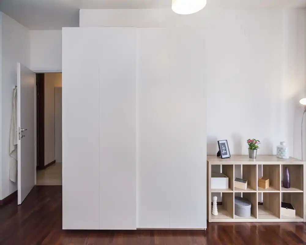 Parete di camera con grande armadio a muro bianco e scaffalatura aperta; pavimento in legno lucido e dettagli decorativi minimal creano un aspetto pulito e moderno.