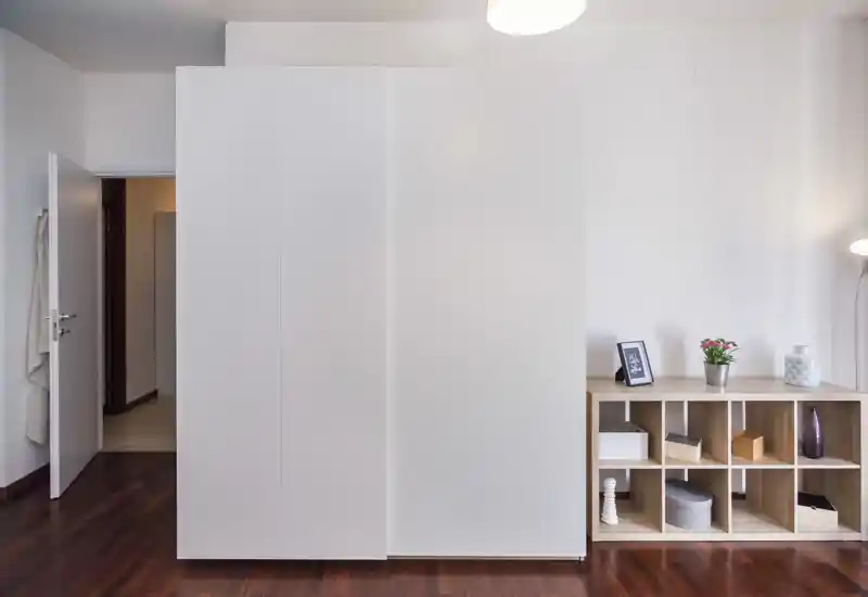 Parete di camera con grande armadio a muro bianco e scaffalatura aperta; pavimento in legno lucido e dettagli decorativi minimal creano un aspetto pulito e moderno.