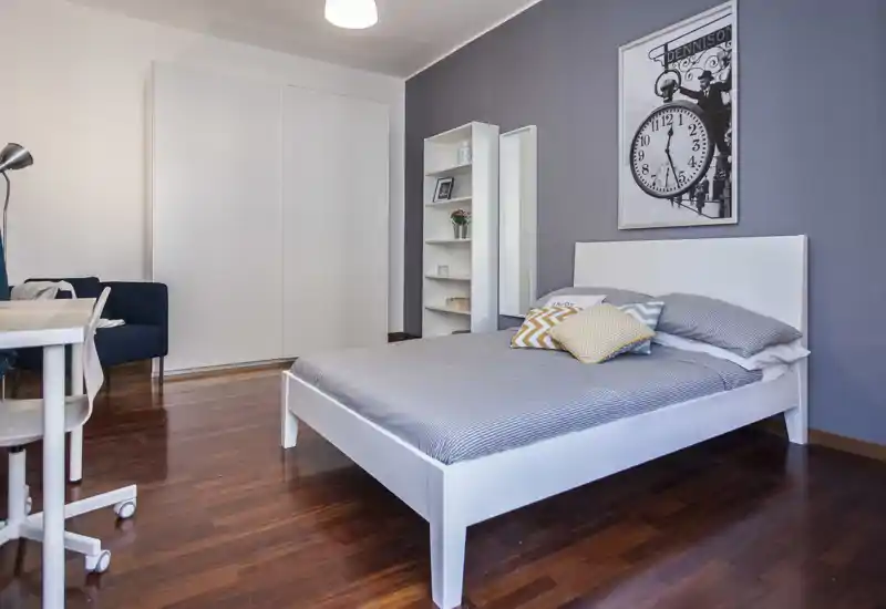 Bright, modern bedroom with a neatly made double bed on warm wooden floors, decorative cushions and minimalist shelving for storage.