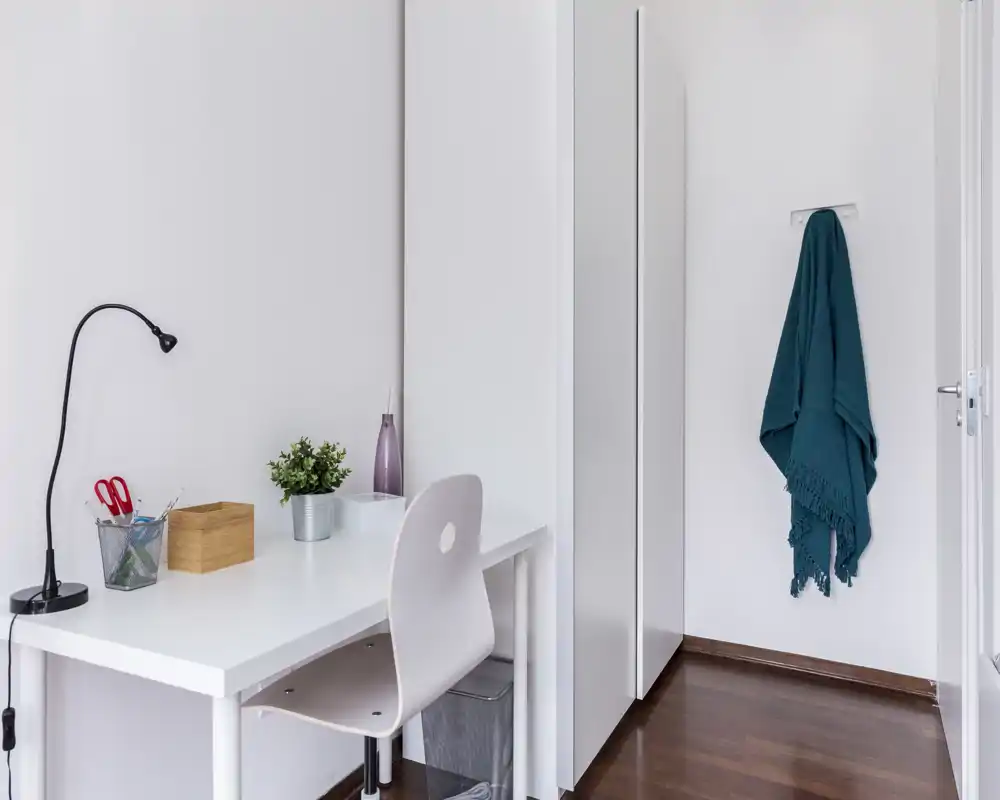 Bright, minimal home-office corner with a white desk, chair, desk lamp and small decorative items; clean and functional study area.