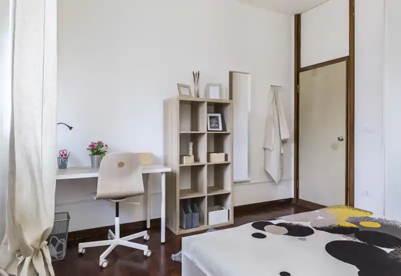 Dormitorio moderno y luminoso con edredón estampado, suelo de madera, escritorio y estantería — bien decorado y con buena luz.