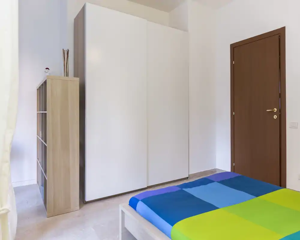 Dormitorio moderno y luminoso con colcha colorida, gran armario blanco y luz natural. Estilo limpio y minimalista, ideal para anuncios de alquiler.