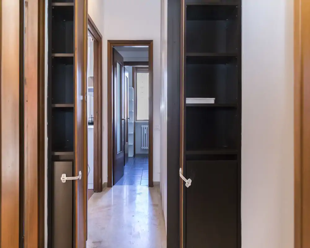 A narrow entrance/hallway with built-in shelving and doors leading to inner rooms; neutral lighting and clean, simple lines suitable for a listing's overview of circulation space.