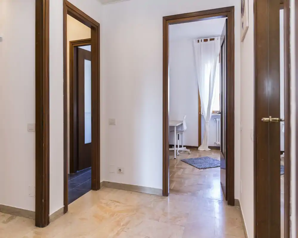 Bright, neutral entrance/hallway with multiple doorways leading to adjacent rooms; polished stone floor and simple white walls provide a clean transitional space.