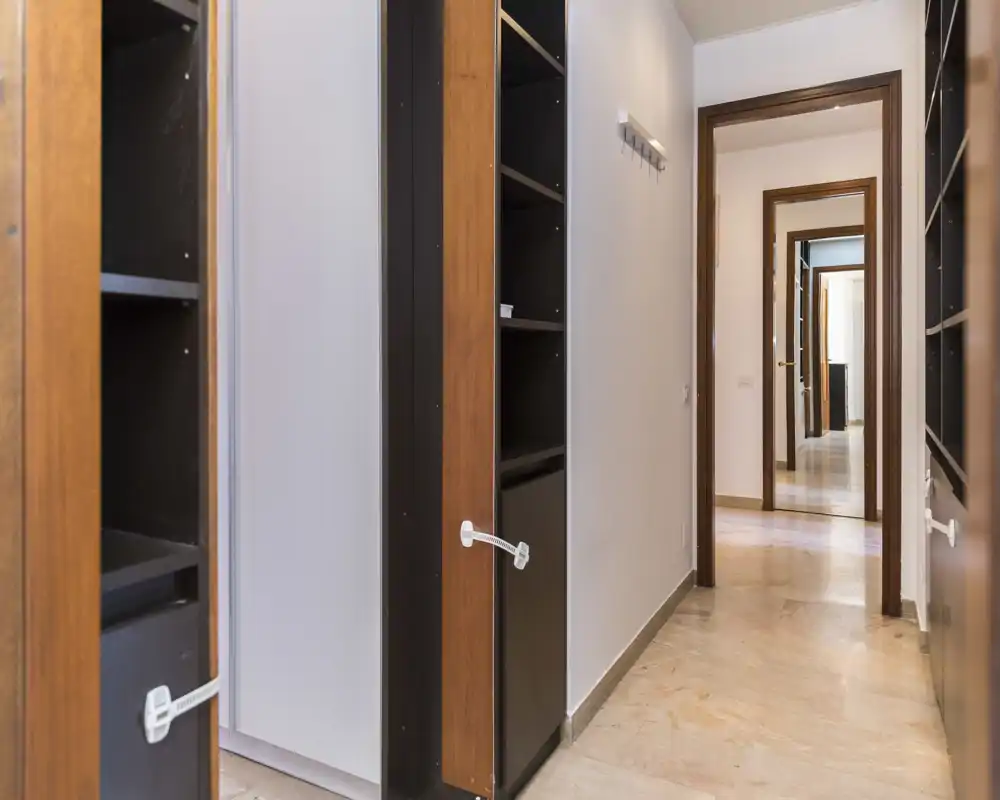 Narrow hallway/entrance with built-in shelving and a light-colored marble floor, well lit and suitable for storage or coat hooks near the doorway.