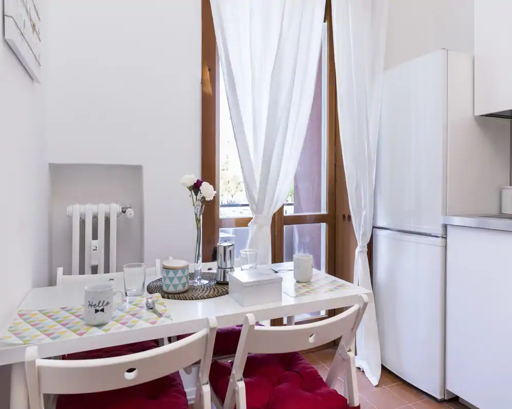 Compact, bright kitchen corner with a small dining table set for two, cheerful placemats and natural light from French-style doors.
