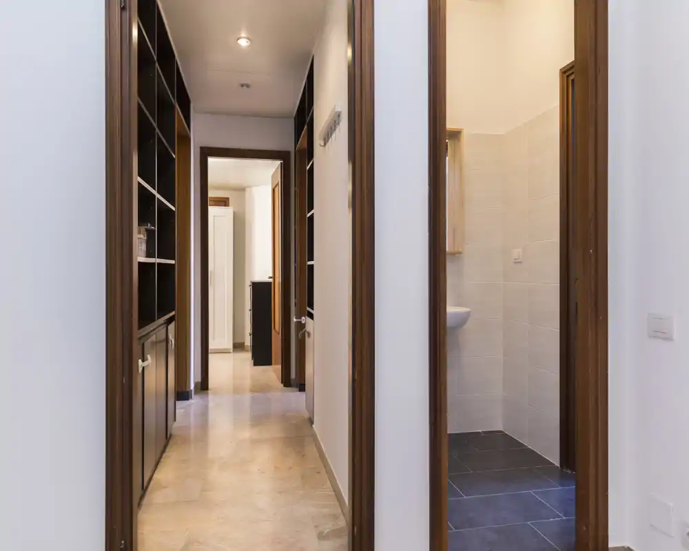 Bright, well-lit entrance hallway with built-in shelving and doors leading to other rooms; neutral tiles and wooden door frames provide a clean, welcoming first impression.